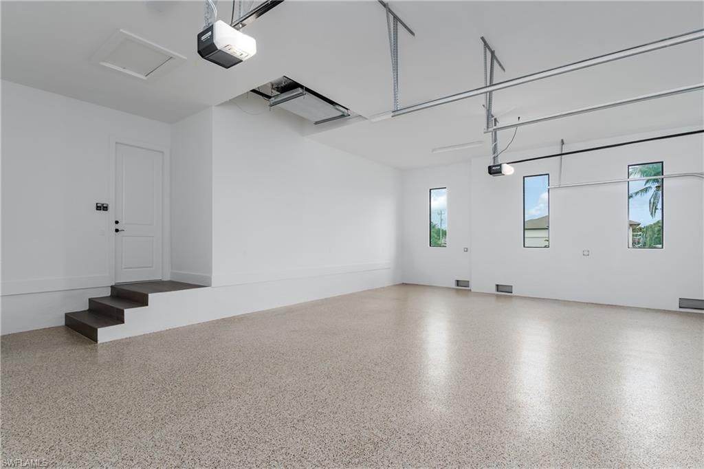 Spacious garage featuring a durable epoxy-coated floor, multiple windows providing natural light, and an interior access door with three steps