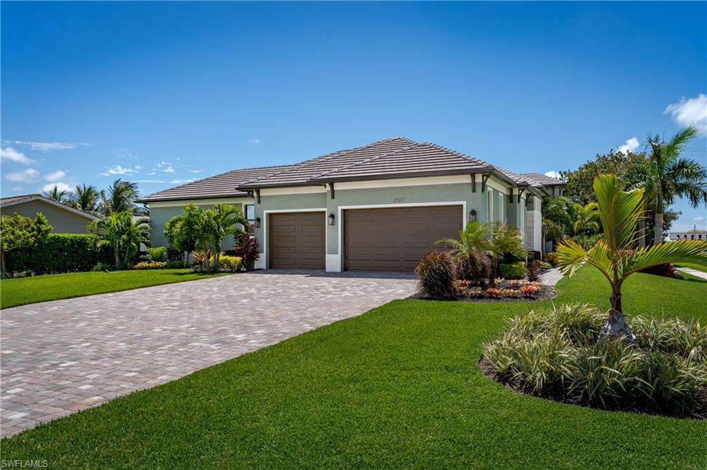 Contemporary exterior featuring a paver driveway, two-car garage, and lush tropical landscaping