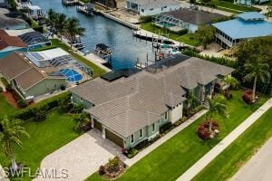 Waterfront property featuring extensive green lawn, mature palm trees, a concrete driveway, and a paved walkway
