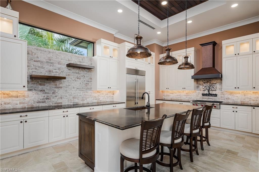 Gourmet kitchen featuring a large central island with seating, white shaker-style cabinetry, a distressed brick backsplash, and undermount lighting