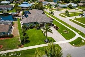 Waterfront property featuring a paver driveway, two-car garage, mature palm trees, and lush green landscaping