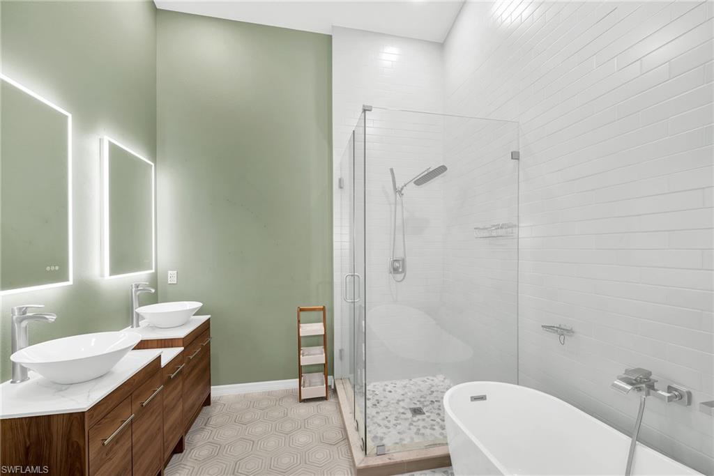 Bathroom featuring a dual vanity with vessel sinks, back-lit mirrors, a frameless glass shower enclosure with a rain shower head, a freestanding soaking tub, and hexagonal floor tiling