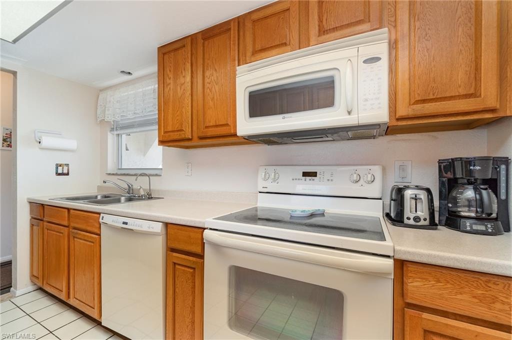 Kitchen featuring wood cabinetry, light-toned countertops, a stainless steel double basin sink, an electric range, and an over-the-range microwave