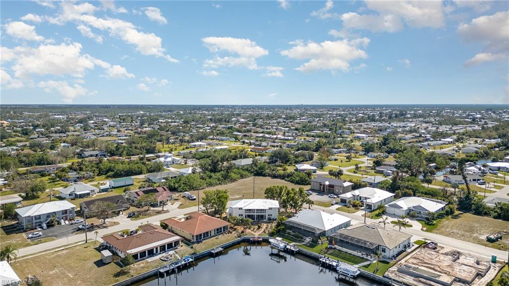 Expansive aerial view showcasing a residential area with a prominent canal, multiple properties with private boat docks, and numerous single-story homes