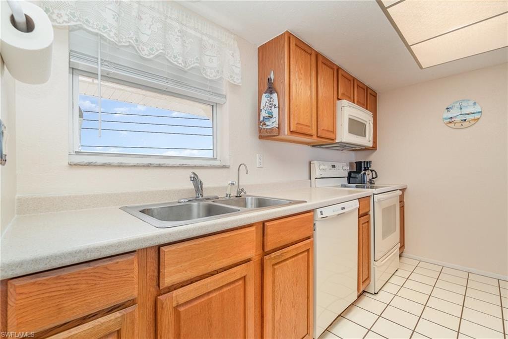 Kitchen featuring light wood cabinetry, a dual basin stainless steel sink, white countertop, and white tile flooring