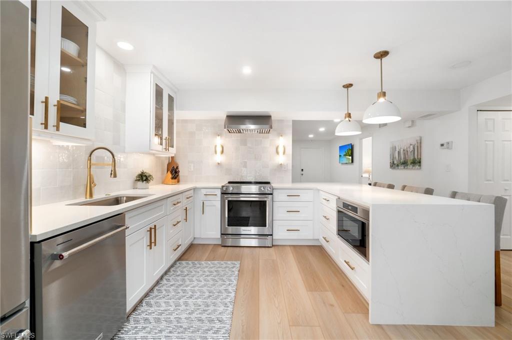 Modern kitchen featuring light wood-finish flooring, white cabinetry with brass hardware, and stainless steel appliances