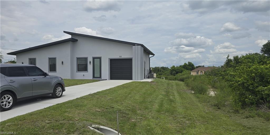 Contemporary grey stucco exterior featuring a dark grey garage door, a modern entry door with a vertical glass panel, and exterior wall sconces