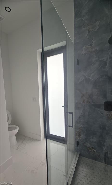 Modern bathroom featuring a frameless glass shower enclosure with matte black hardware, large format marble-look floor tiles, dark-toned shower wall tiling, and a black-framed privacy door