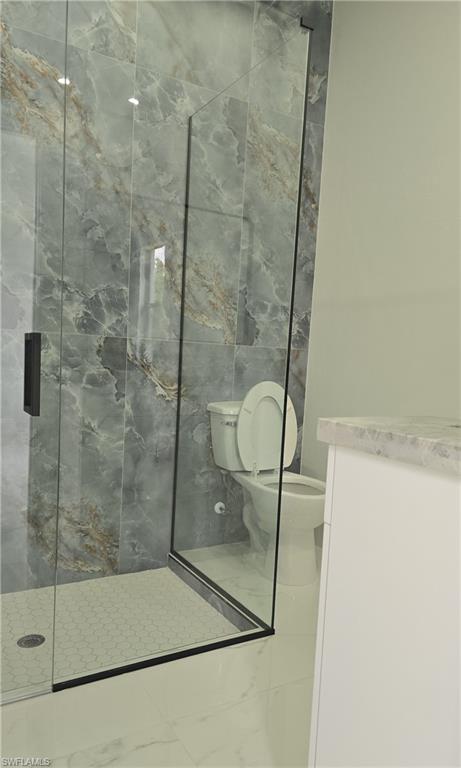 Glass-enclosed shower featuring large format tile surround with natural stone appearance and hexagonal mosaic floor