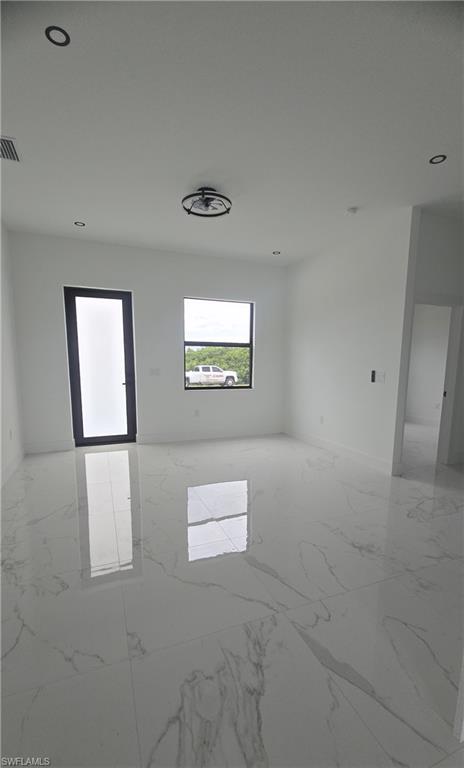 Spacious room featuring polished white tile flooring with gray veining, a black-framed glass-paneled door, and recessed lighting