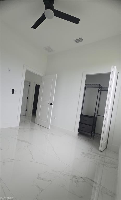Spacious room with large-format marble-look tile flooring, crisp white walls, and a contemporary black ceiling fan