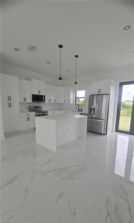 Modern kitchen featuring a large center island with a solid surface countertop, white shaker cabinetry, and stainless steel appliances