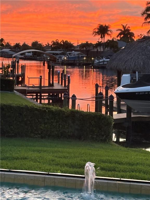 Waterfront property featuring a private boat dock, adjacent boat lift with thatched roof canopy, and a fountain feature in the foreground