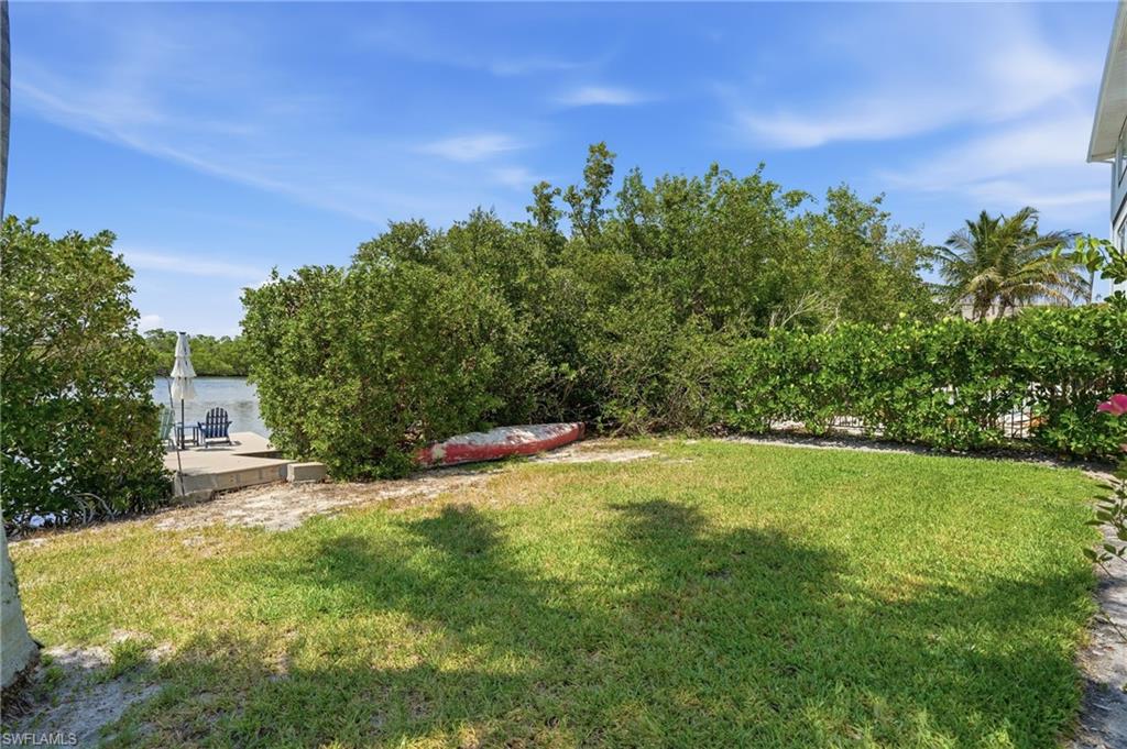 Green lawn area with a concrete patio overlooking the water, featuring lush surrounding foliage and a clear sky - Virtually Edited Image