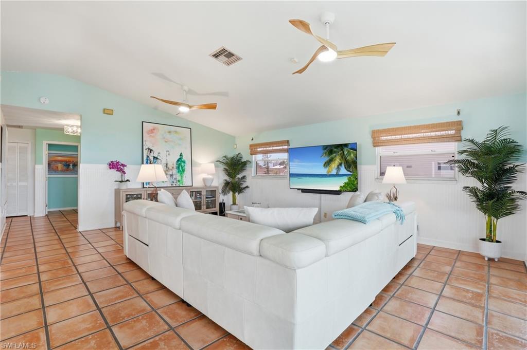 Living area with vaulted ceilings, terracotta-style floor tiling, paddle-blade ceiling fans, and a partial wainscoting wall finish - Virtually Edited Image