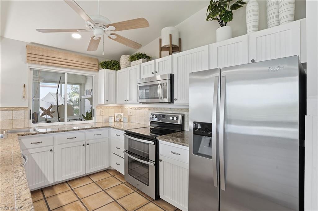 Kitchen featuring white beadboard cabinetry, granite countertops, tile backsplash, stainless steel appliances, and a vaulted ceiling with a ceiling fan - Virtually Edited Image
