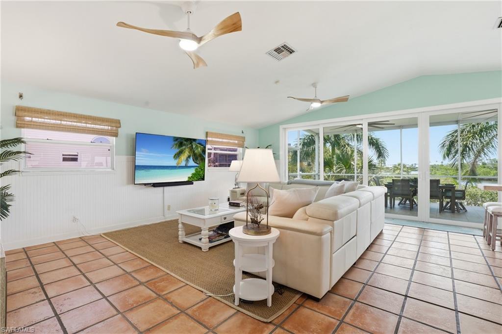 Spacious living area featuring terra cotta tile flooring, vaulted ceilings with modern ceiling fans, and a partial wainscoting wall finish - Virtually Edited Image