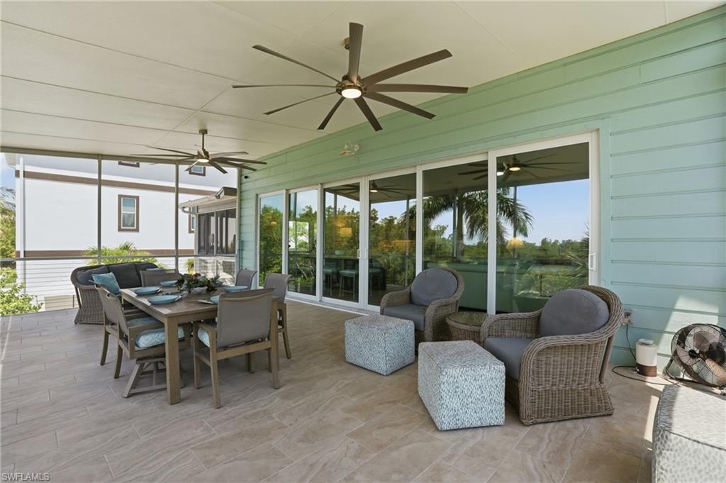 Expansive screened patio featuring large format tile flooring, a pale green siding exterior, multiple ceiling fans with integrated lighting, and a full wall of sliding glass doors - Virtually Edited Image