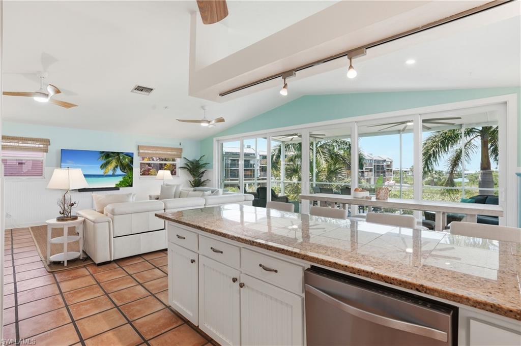 Open-concept living space featuring a vaulted ceiling, track lighting, and a kitchen island with stone-finish countertops - Virtually Edited Image