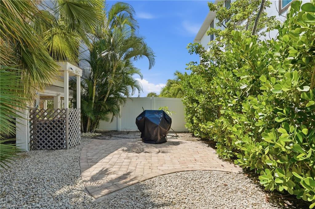 Private outdoor patio featuring paver stones, surrounding gravel, and mature landscaping - Virtually Edited Image