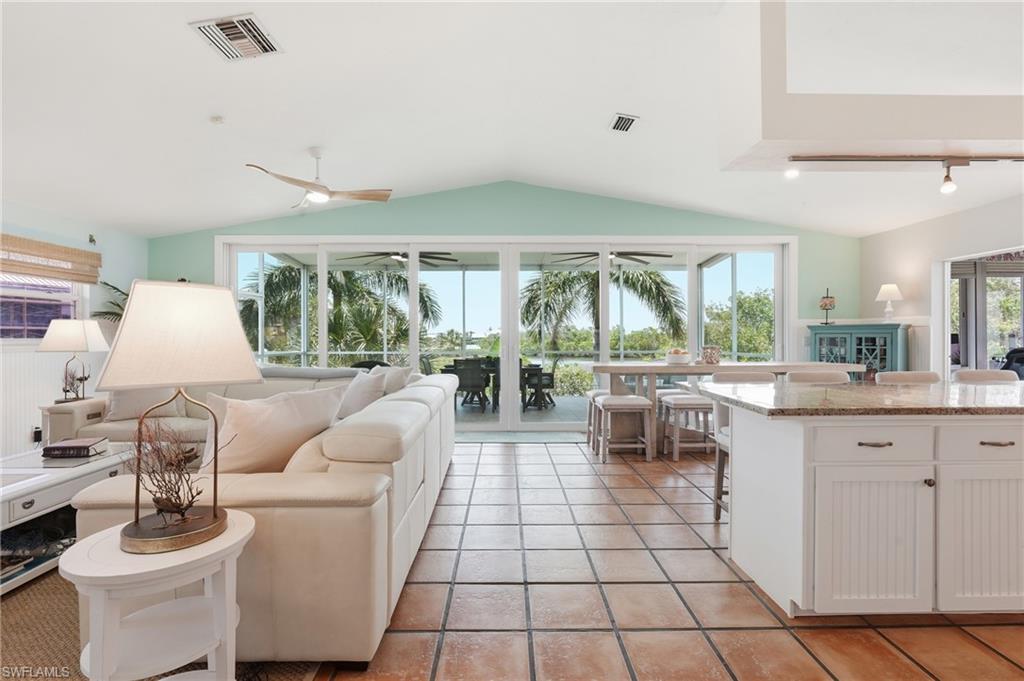 Spacious living area featuring terra cotta tile flooring, vaulted ceilings, and a kitchen island with a light-toned countertop - Virtually Edited Image