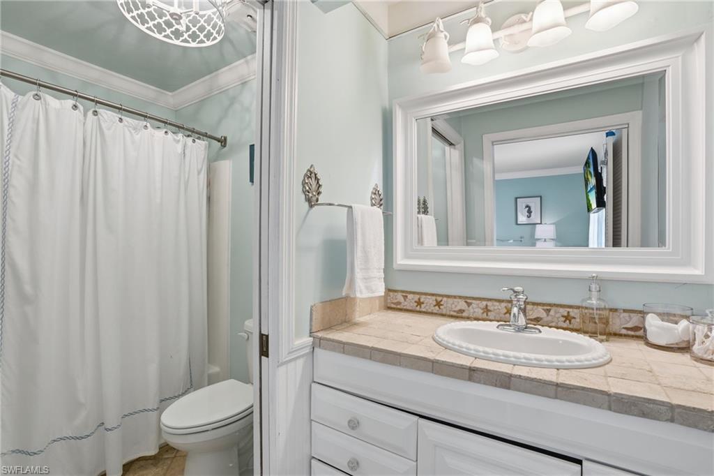 Bathroom featuring a white vanity with an integrated sink, tiled countertop, and a framed mirror - Virtually Edited Image