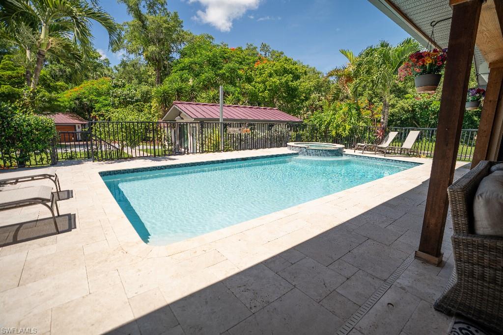 Outdoor swimming pool with integrated spa, surrounded by stone paver decking and a black metal fence