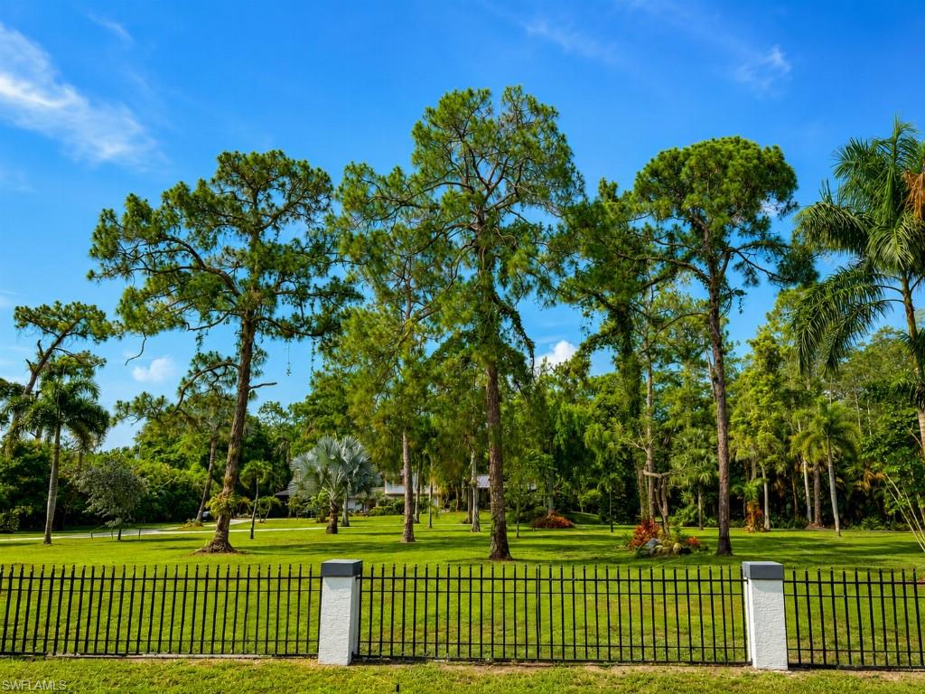 Expansive green lawn framed by a black metal fence with stone-clad posts