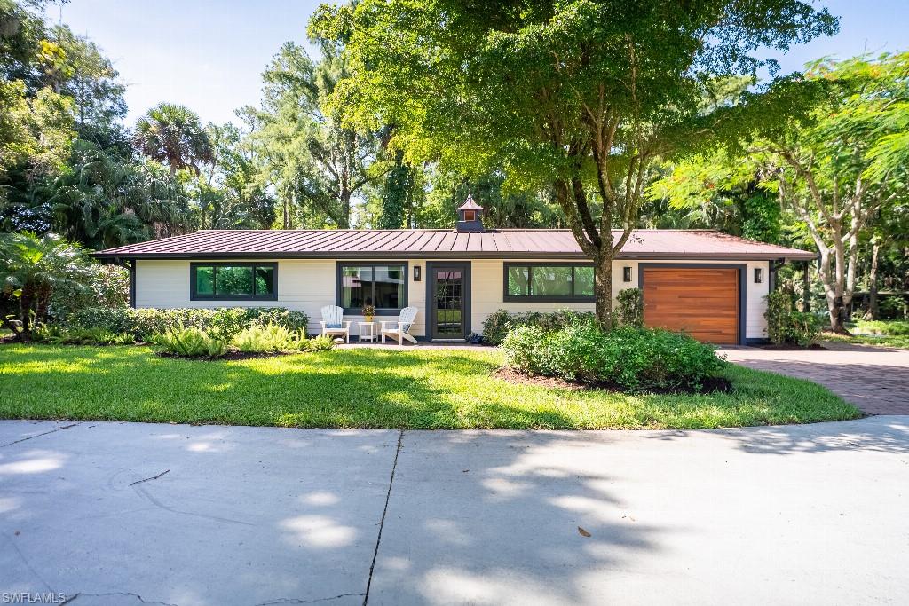 Single-story residence featuring a metal roof, light-toned exterior siding, and a wooden garage door
