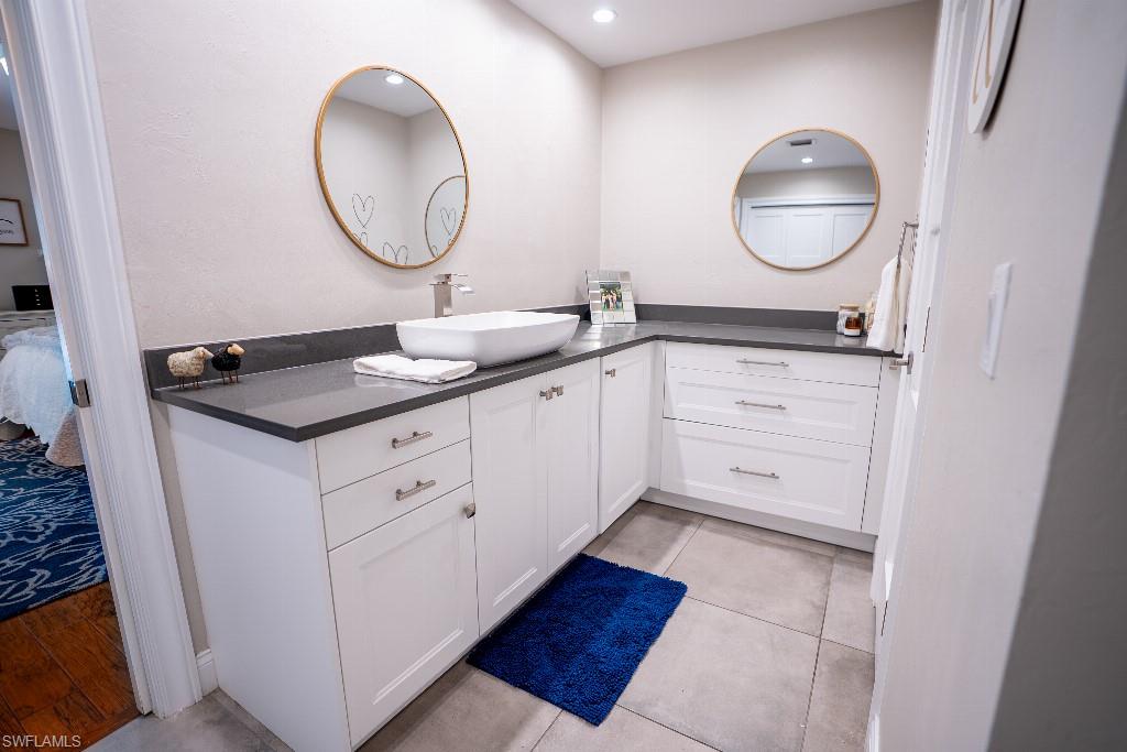 Bathroom vanity featuring white cabinetry, a dark countertop, a vessel sink with a chrome faucet, and tile flooring