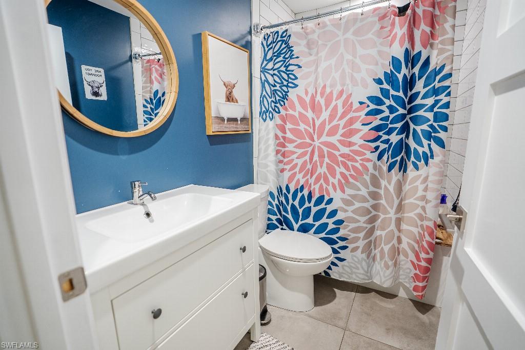 Bathroom featuring a white vanity with integrated sink, coordinating white toilet, and tile flooring
