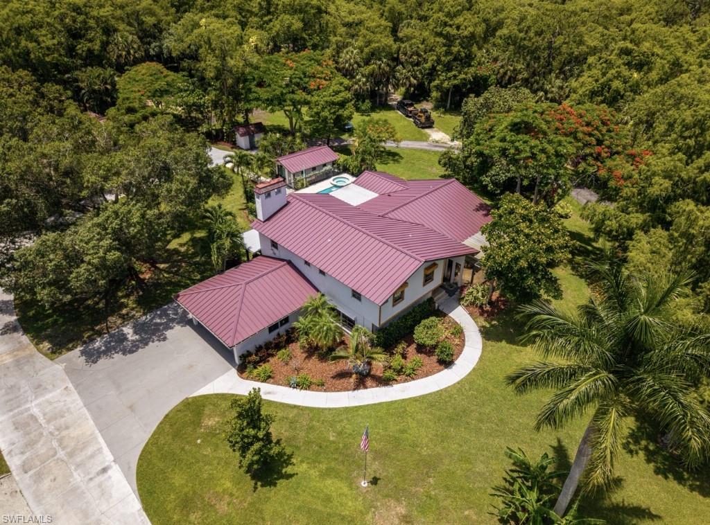 Expansive property featuring a red metal roof, mature tropical landscaping, a private swimming pool, a detached outbuilding, and a paved driveway with ample parking