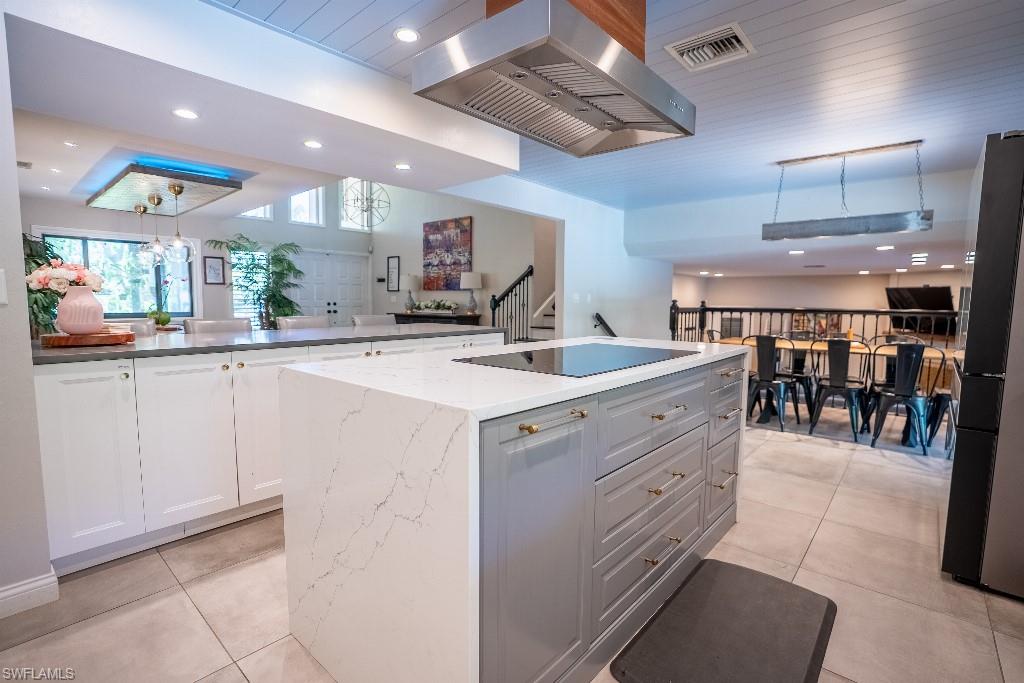 Kitchen featuring a large central island with an integrated cooktop, stone countertops, and light gray cabinetry with brass hardware