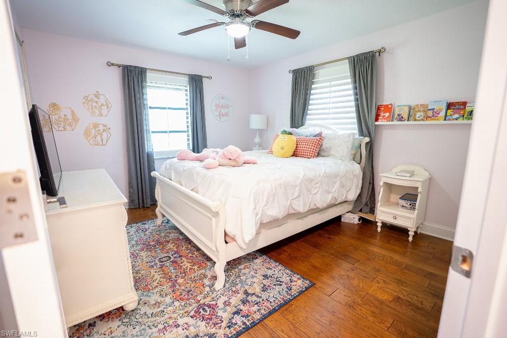 Hardwood flooring, a ceiling fan, and a window with blinds and drapes define this room