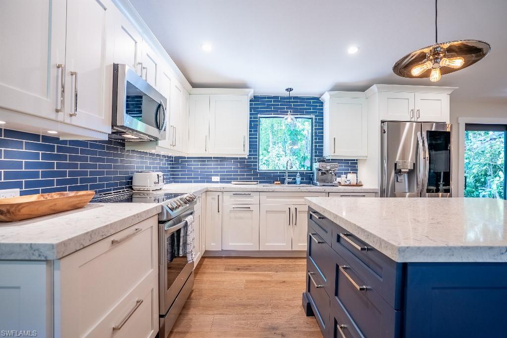 Gourmet kitchen featuring white shaker cabinetry, blue subway tile backsplash, stainless steel appliances, light wood-finish flooring, and a contrasting blue island with a light countertop