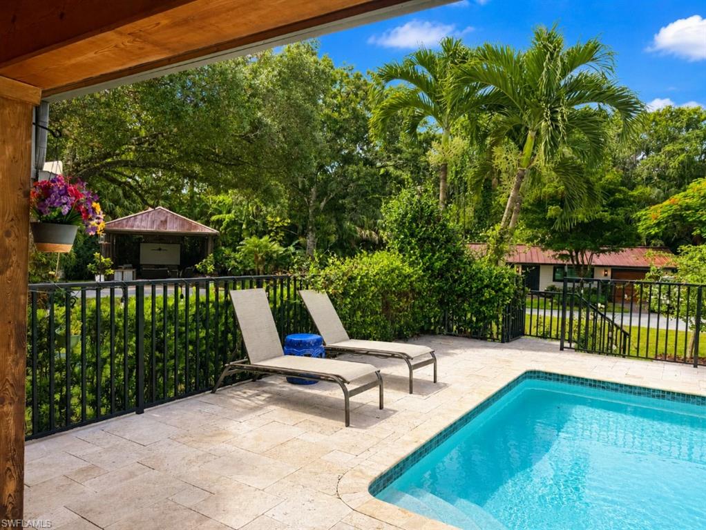 Outdoor living area featuring a rectangular pool with tiled coping, a spacious paver patio, and black metal fencing