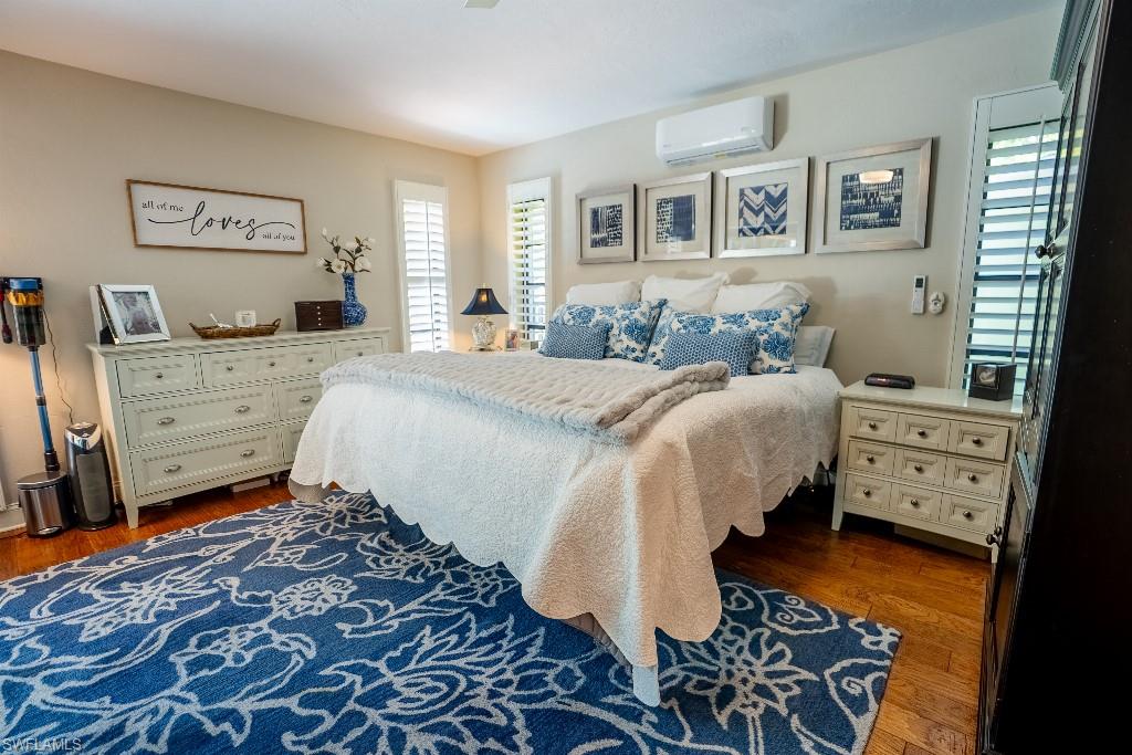 Hardwood flooring extends throughout this room, featuring plantation shutters on the windows and a wall-mounted climate control unit