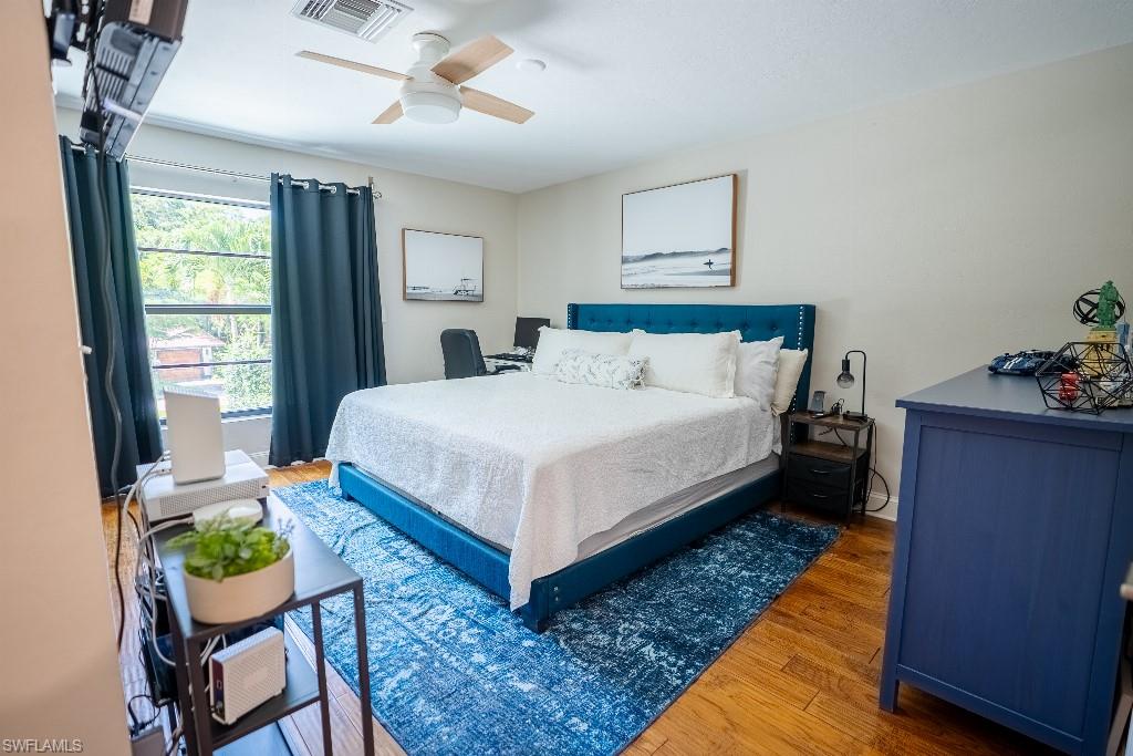 Hardwood-finish flooring featuring a ceiling fan, window with privacy curtains, and light-toned walls