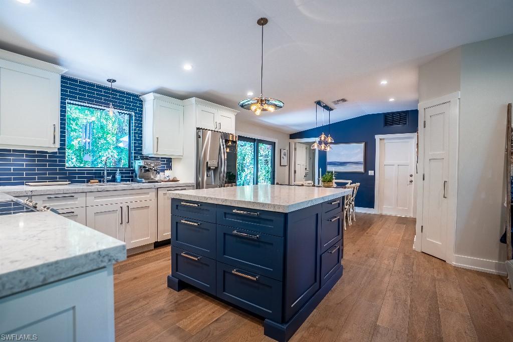 Spacious kitchen featuring a central island with countertop, white perimeter cabinetry, blue subway tile backsplash, and light wood-finish flooring