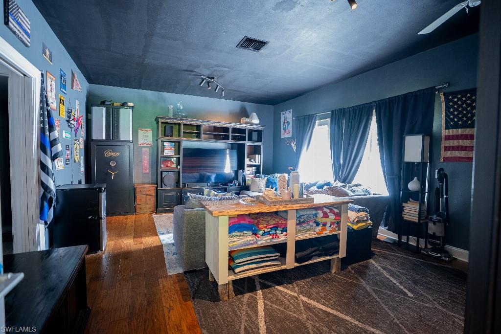 Living area featuring hardwood flooring, a ceiling fan, track lighting, and a window with dark curtains