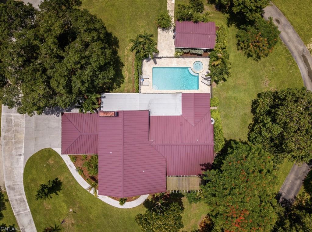 Aerial perspective showcasing a property with a red metal roof, a rectangular swimming pool, and an integrated spa