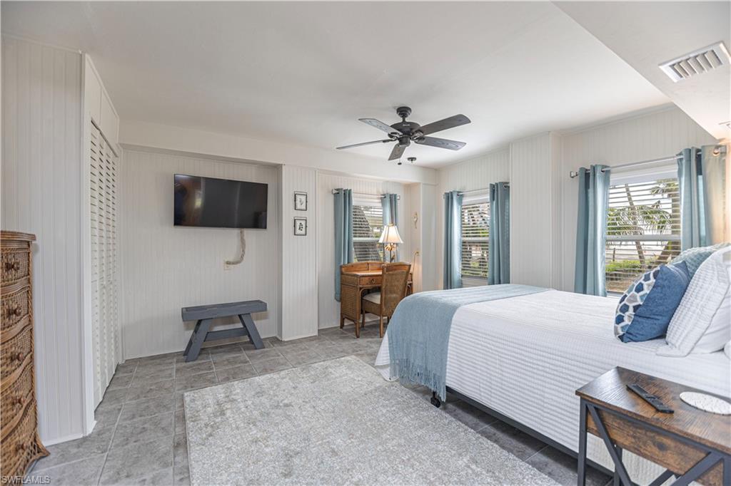 Spacious bedroom featuring tile flooring, white vertical plank accent walls, and multiple windows with horizontal blinds - Virtually Edited Image