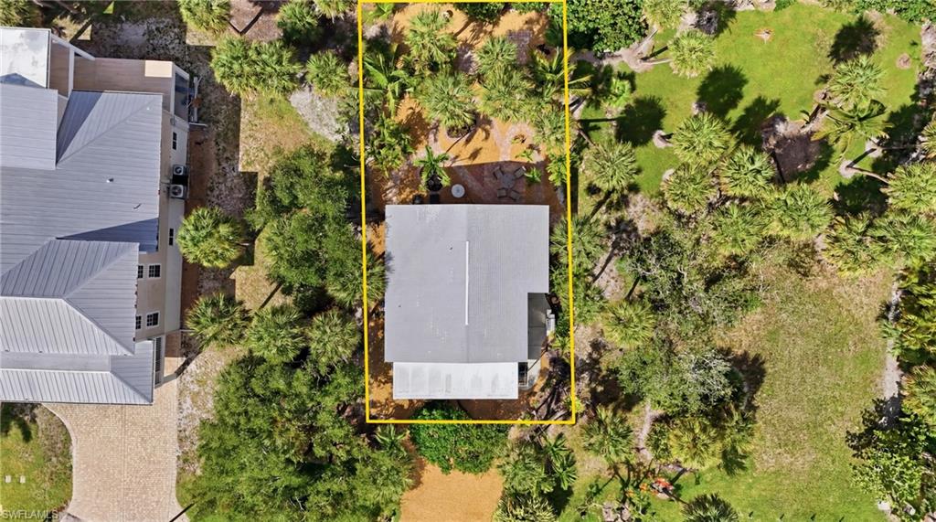 Property parcel featuring a light-colored roof structure, surrounded by mature trees and lush vegetation - Virtually Edited Image