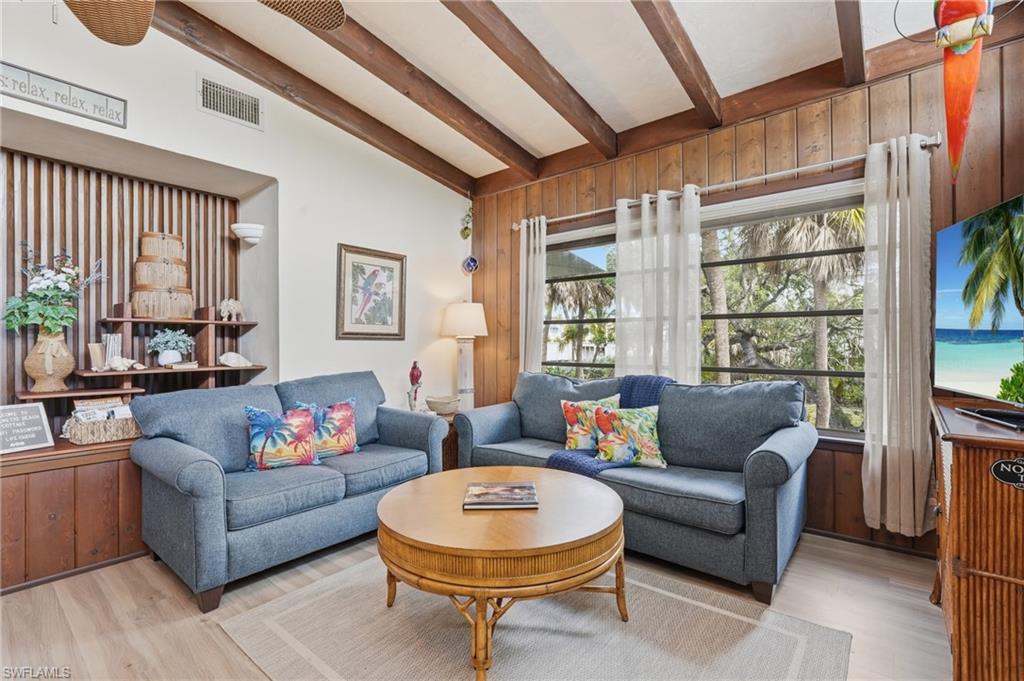 Living space featuring vaulted ceilings with exposed wood beams, wood-finish wall paneling, and multiple windows - Virtually Edited Image