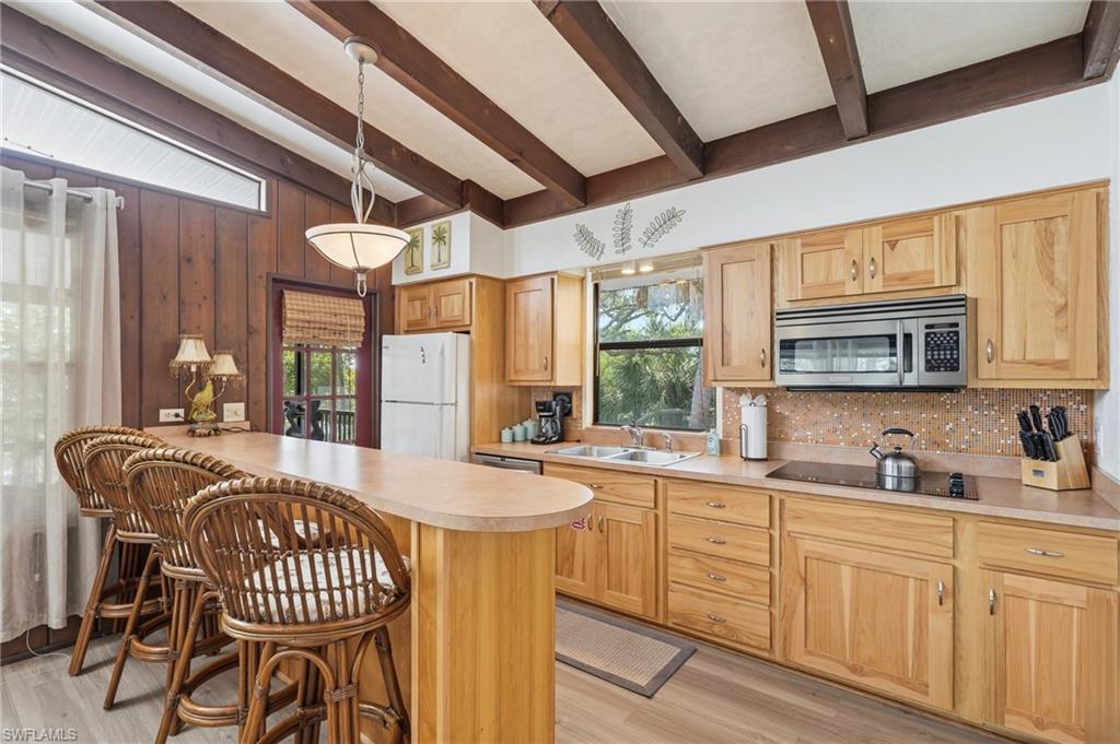 Kitchen featuring wood-finish cabinetry, a breakfast bar, and a built-in stainless steel microwave - Virtually Edited Image