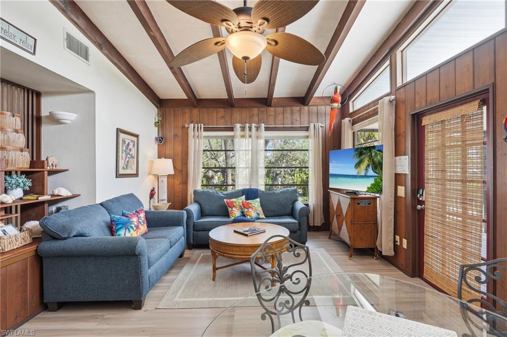 Living area featuring vaulted ceilings with exposed wood beams, wood-finish wall paneling, and light wood-finish flooring - Virtually Edited Image