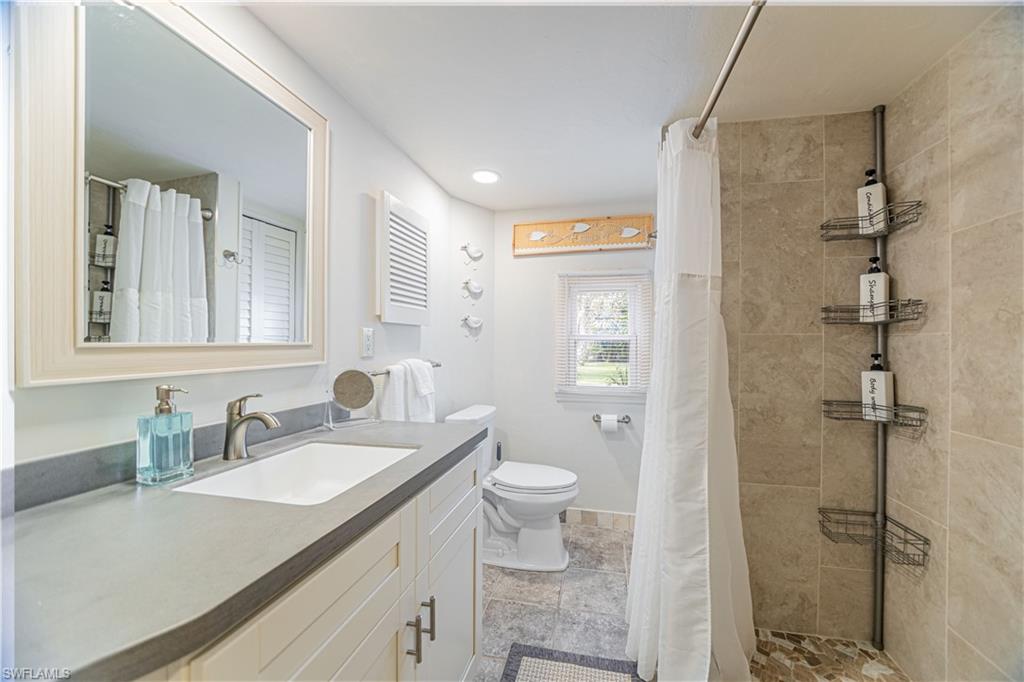 Bathroom featuring a vanity with a rectangular undermount sink, a framed mirror, and a window - Virtually Edited Image