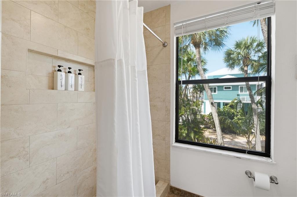 Shower enclosure featuring beige tile walls, a built-in recessed niche, and a window with blinds - Virtually Edited Image