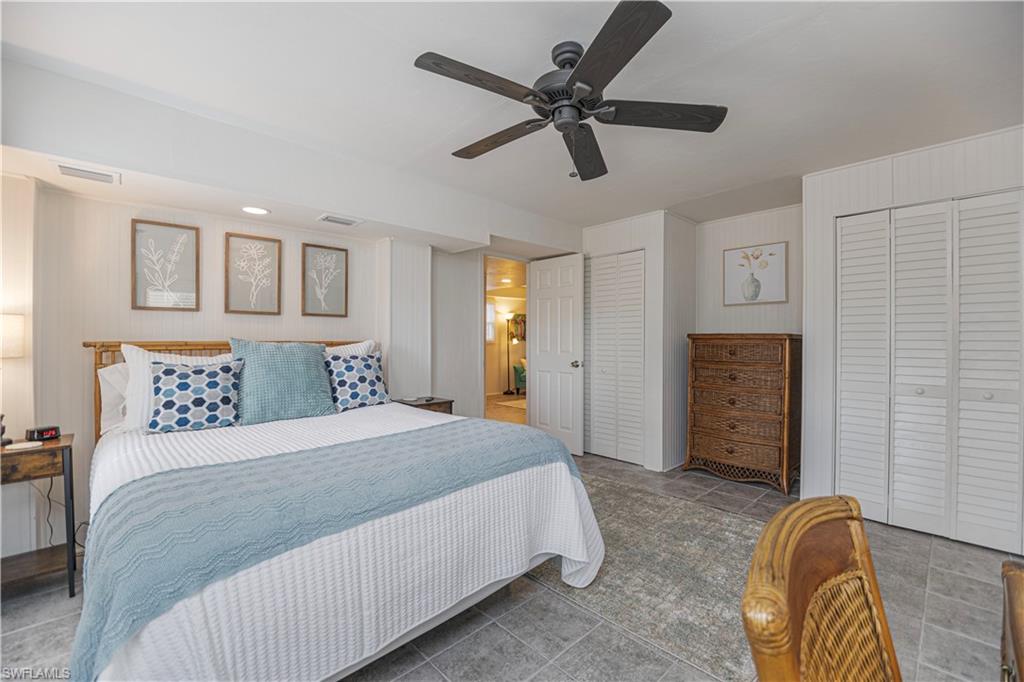 Spacious room featuring gray tiled flooring, a dark-toned ceiling fan, recessed lighting, and two sets of louvered bifold closet doors - Virtually Edited Image