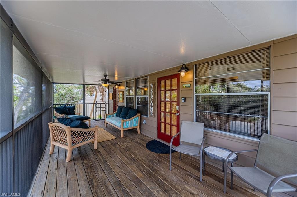 Spacious screened porch featuring wood-finish flooring, a ceiling fan, and multiple windows - Virtually Edited Image